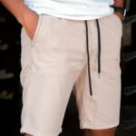 Close-up of a person wearing casual beige shorts with hands in pockets.