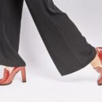 Stylish red high heels paired with black pants on a clean white background.