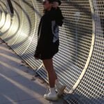 Fashionable woman in black hoodie by a modern metal fence in urban setting.