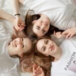 Three young women lying on a bed, smiling and enjoying casual moments indoors.