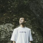 A man looks upwards in a natural, rocky setting conveying exploration and introspection.