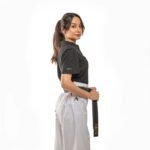 Confident woman posing in martial arts uniform holding a black belt in studio