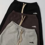 Three neatly stacked pairs of sweatpants with drawstrings in stylish neutral colors.