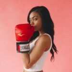 Stylish woman posing with red boxing gloves on a pink background, exuding confidence and fitness.