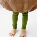 Adorable child's legs wearing green leggings standing barefoot on a white surface.