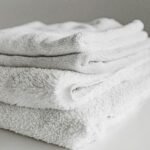 Neatly folded clean white towels stacked on a surface, perfect for home or spa use.