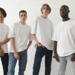 A group of four diverse men modeling white t-shirts and jeans in a studio setting.